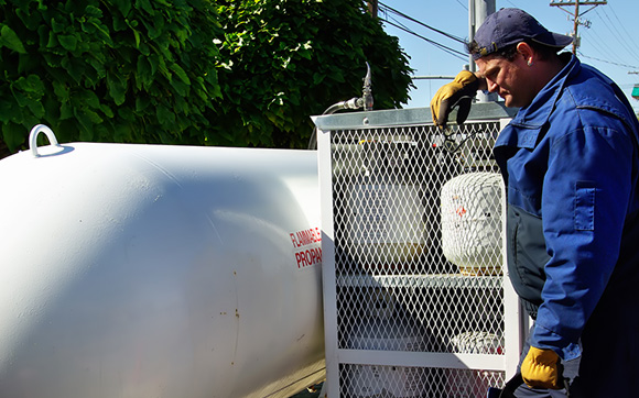 Worker standing in front of large propane tanks and a rack with many smaller ones